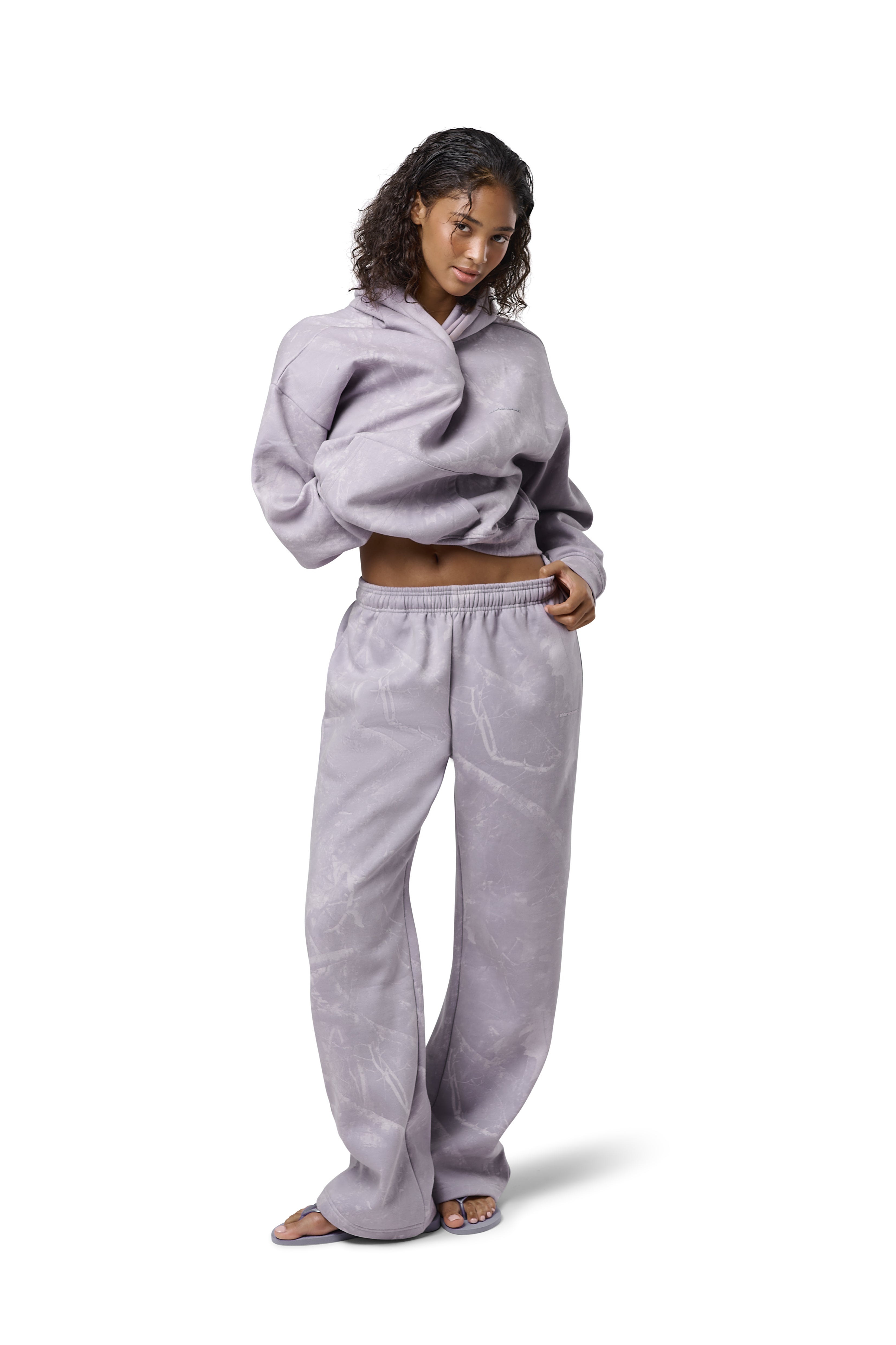 Lilac high-waisted straight-leg sweatpants with subtle twig camo print, elasticated drawstring waist, and embroidered Sisters & Seekers logo. Soft cotton-blend fabric in sizes 2XS–3X, available in Petite, Regular, and Tall lengths